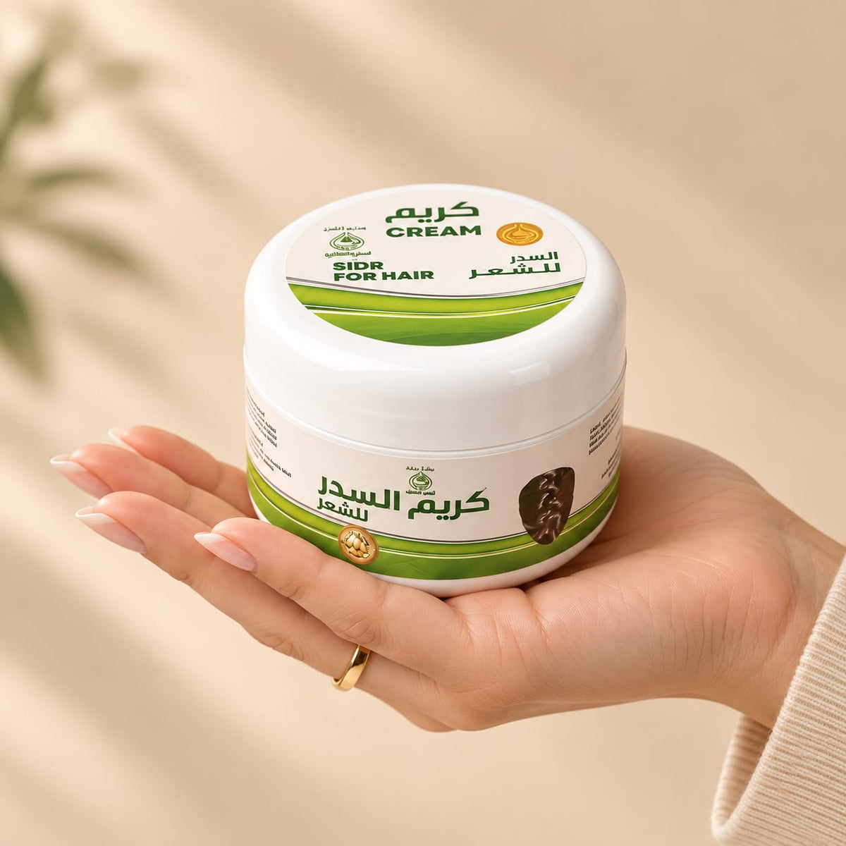 A hand holding a white jar of Al Sidr Cream for hair with green and gold accents. The label features Arabic text reading 'Al Sidr Cream for hair' and 'Hair Repair Cream' with a small gold seal.
