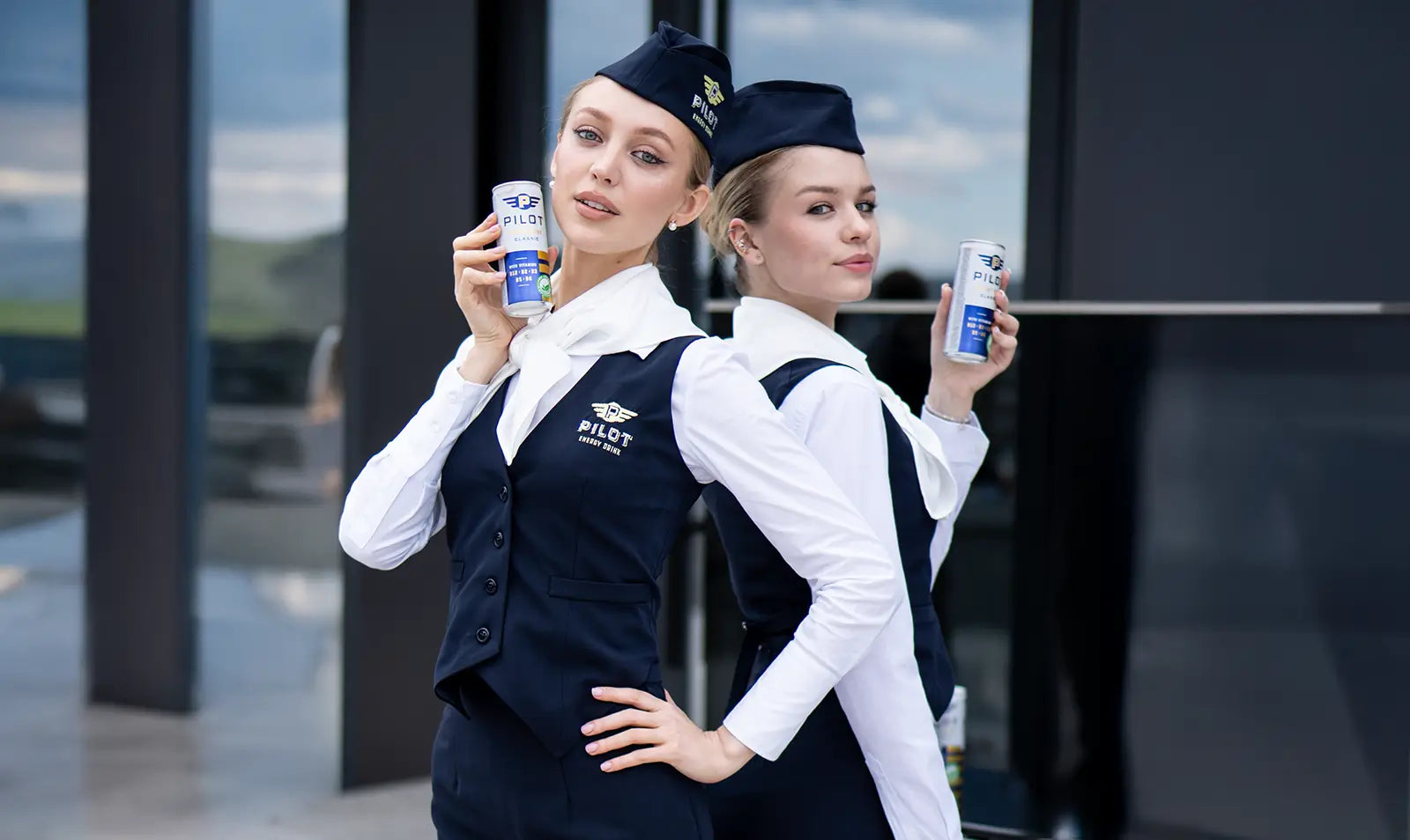 Two flight attendants holding PILOT Energy Drink in front of a building