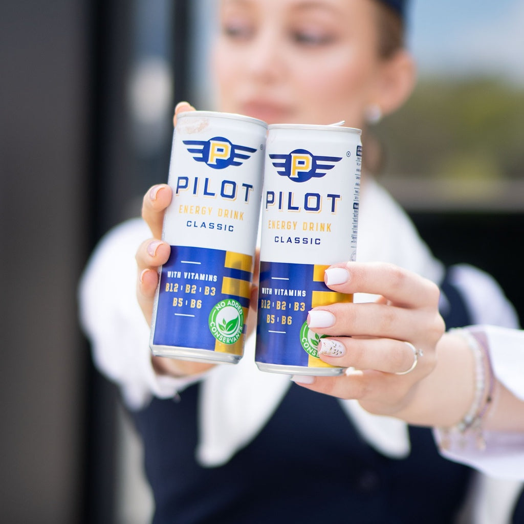 Promoter holding two cans of Pilot Energy Drink with a blurred background