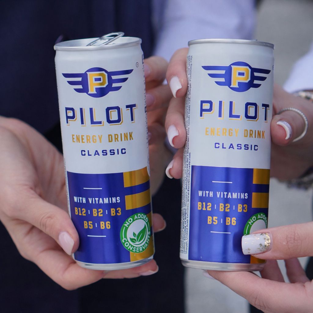 Two cans of PILOT Energy Drink Classic held by hands against a blurred background